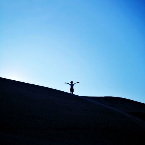 Low angle view of silhouette kid standing against clear blue sky