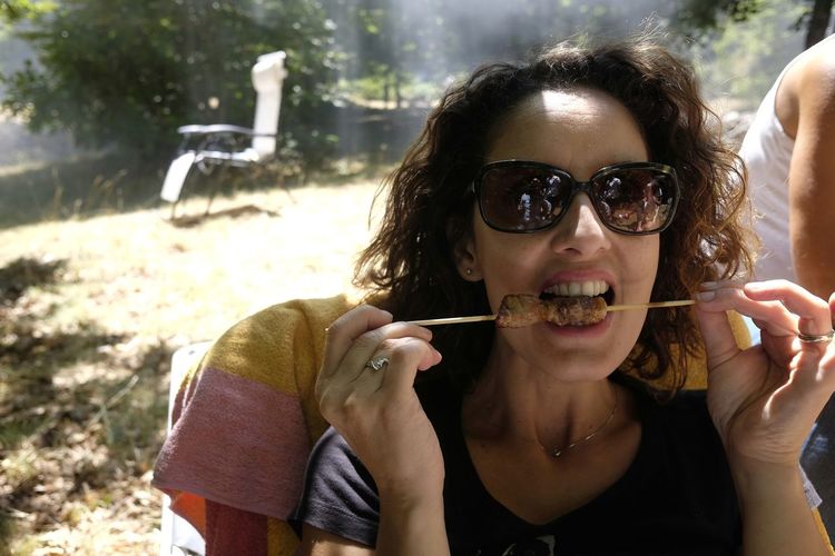 Woman eating arrosticini on field during sunny day
