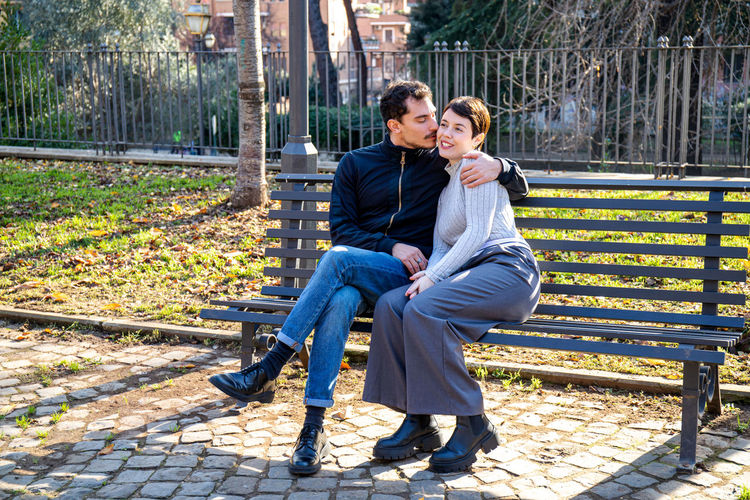 The young couple is sitting on a bench in the park in rome. beautiful couple kisses in the park.