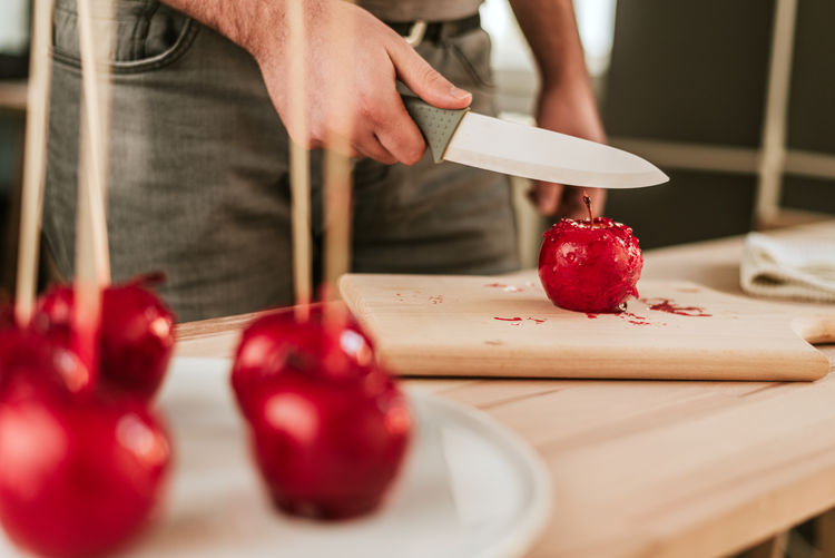 Midsection of man cutting caramelized apple on cutting board