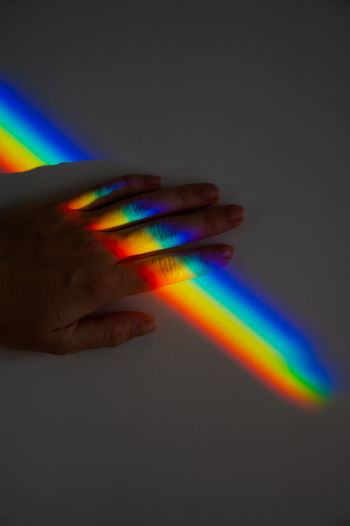 Cropped hand of person on wall with rainbow