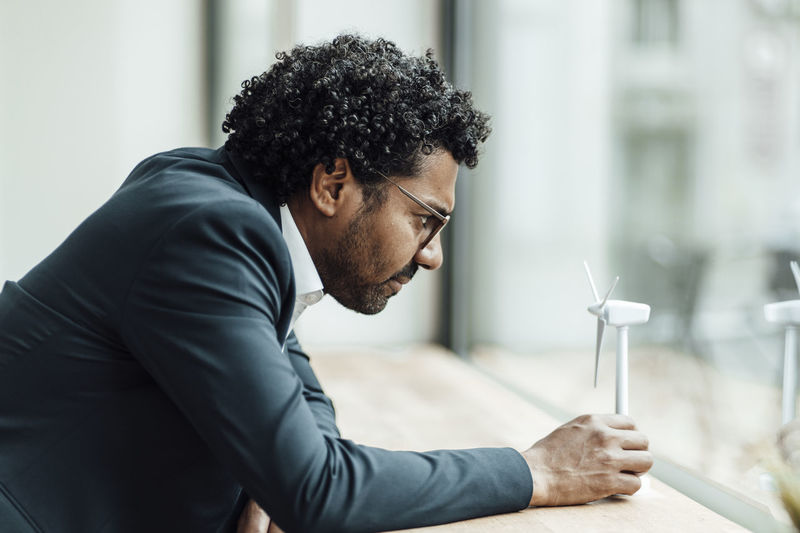 Male professional leaning on desk while examining wind turbine model in office
