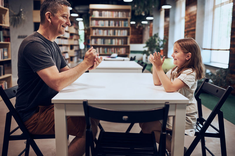 Father playing rock, paper, scissors game with her daughter in public library. family time