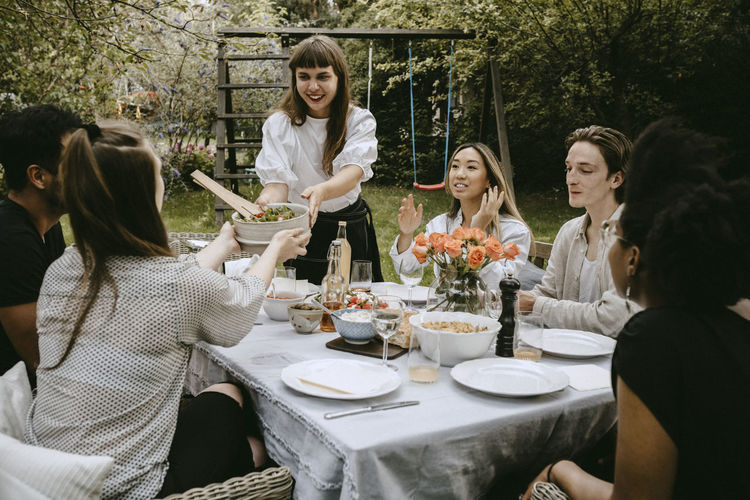 Smiling woman passing food bowl to female friend over table during garden party