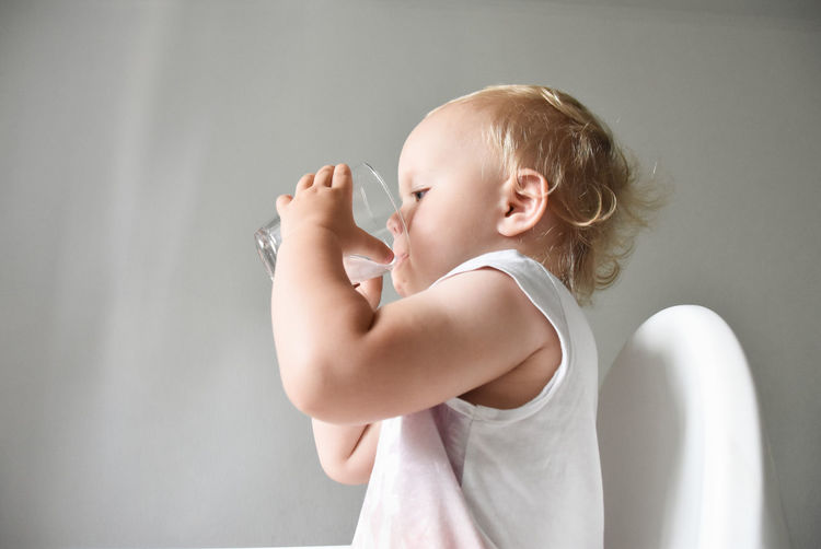 Cute baby girl  against white background drinking water 