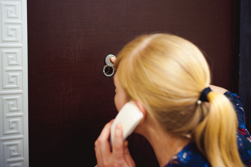 Rear view of woman talking on telephone while standing against door