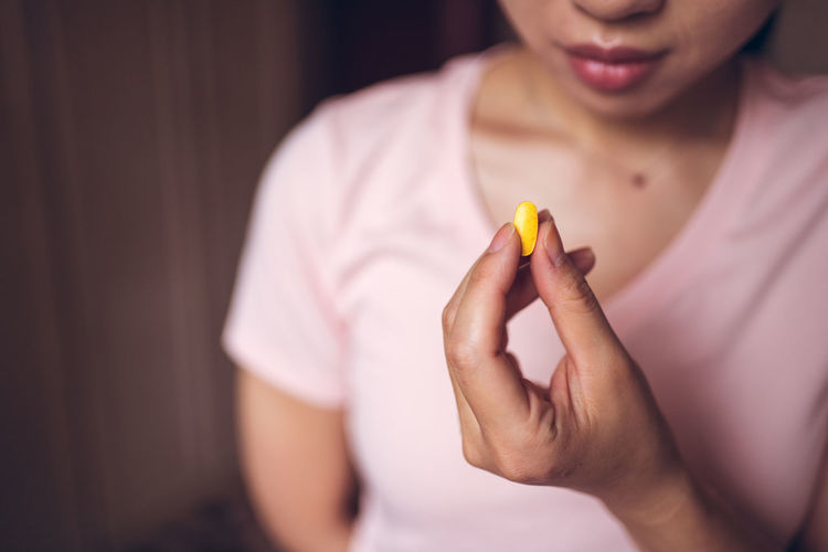 Crop unrecognizable healthy female showing bright yellow vitamin pill during health care routine at home