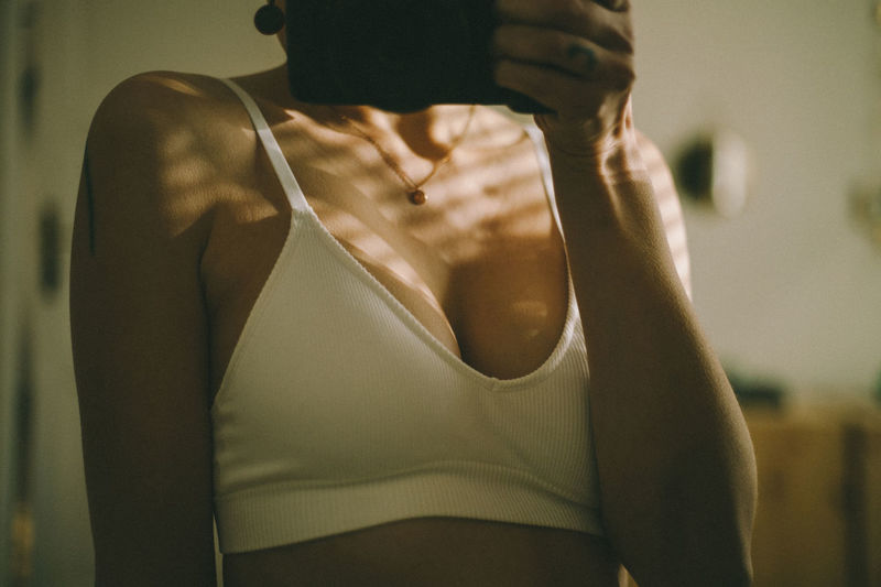 Midsection of woman in the bra in the mirror, standing at home.