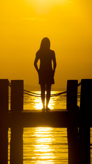 Silhouette woman standing on jetty against sea during sunset