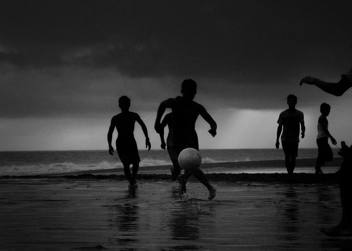 Silhouette children playing on beach against sky