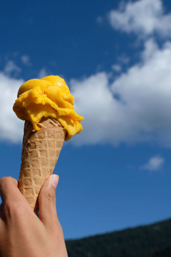 One hand holds original homemade italian ice cream waffle cones with two scoops of mango ice cream.