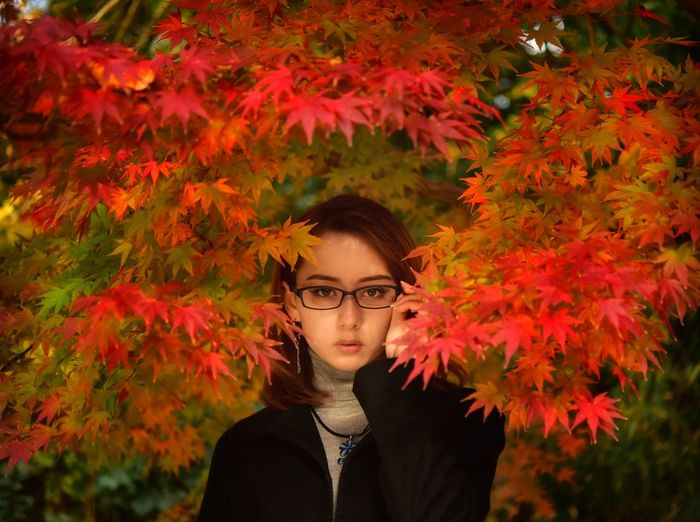 Portrait of young woman standing by plants during autumn