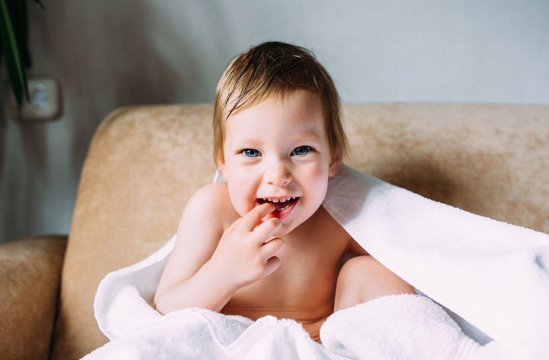 Cute baby in a big white towel. holds fingers in the mouth.