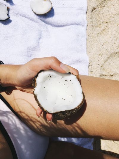 Midsection of woman holding coconut shell at beach during sunny day