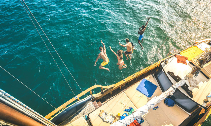 High angle view of friends jumping into sea from sailboat