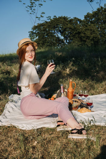 Candid portrait of young red-haired woman lying on a picnic blanket near flowers and basket of food