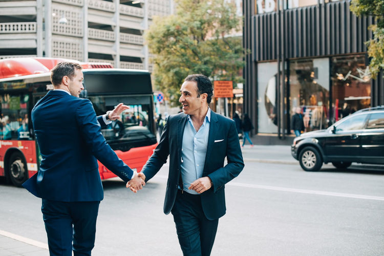 Mature businessman greeting male colleague while walking on street in city