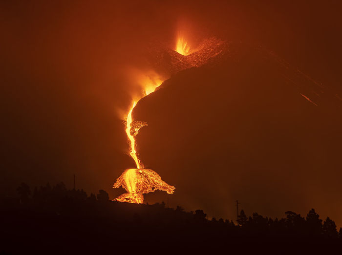 Breathtaking scenery of hot bright orange lava pouring out of erupting cumbre vieja volcano against dark night sky in la palma island