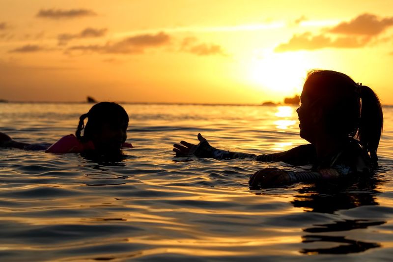 People swimming in sea against sky during sunset
