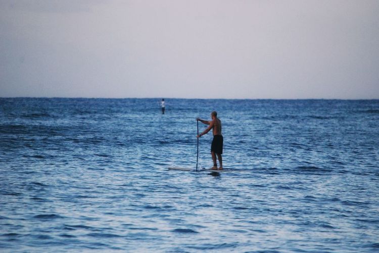 Man paddleboarding in sea against sky