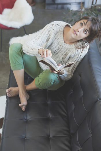 High angle view of woman with book relaxing on sofa at home