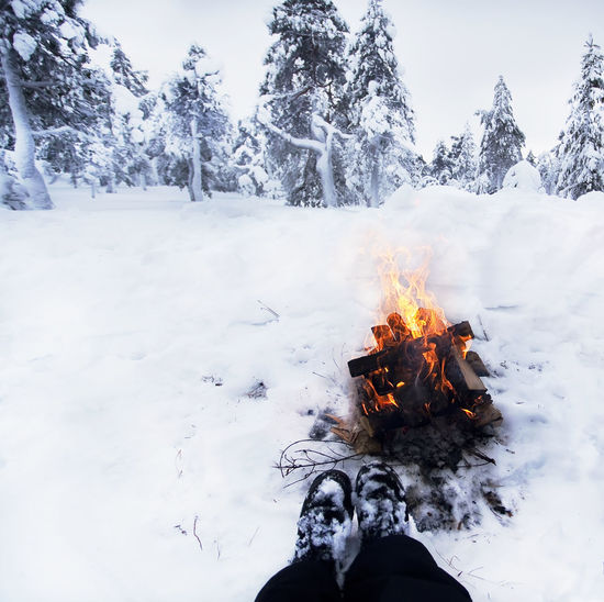 Low section of person against bonfire on snow covered field