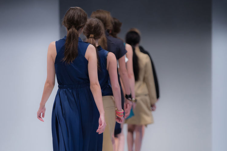 Rear view of fashion models walking in row on stage