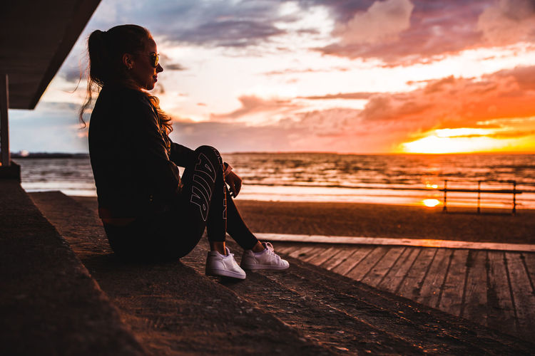 Woman sitting on beach against sky during sunset