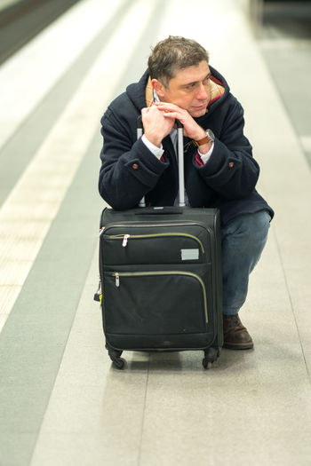 Man with luggage sitting at railroad station platform