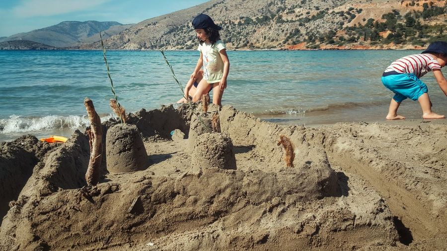 Siblings playing by sandcastle at beach