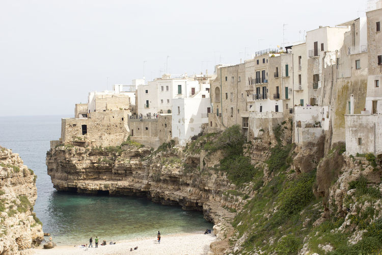 Buildings on cliff by sea at polignano a mare against sky