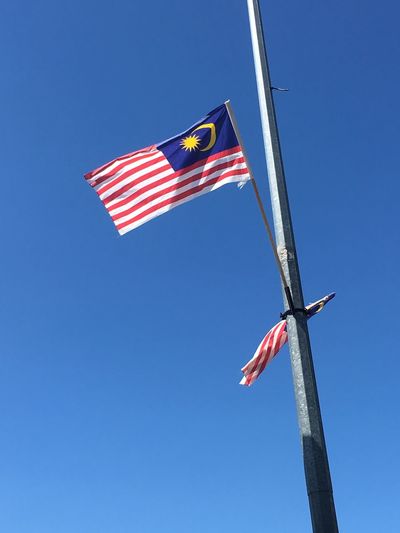 Low angle view of malaysian flags on pole against clear blue sky