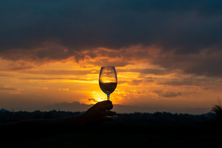 Human hand holding wine glass sky during sunset