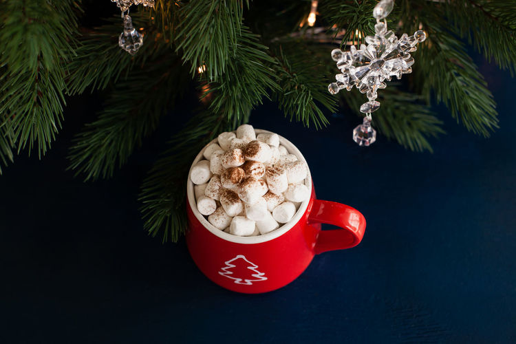 Christmas hot chocolate with marshmallows in a red mug with a garland on the background.