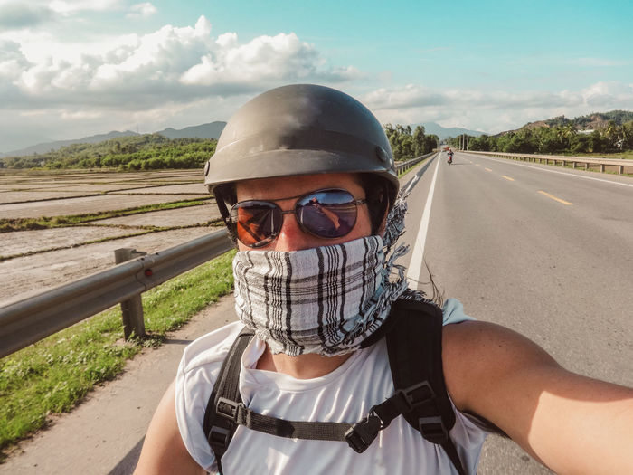 Portrait of man wearing sunglasses and helmet on road against sky