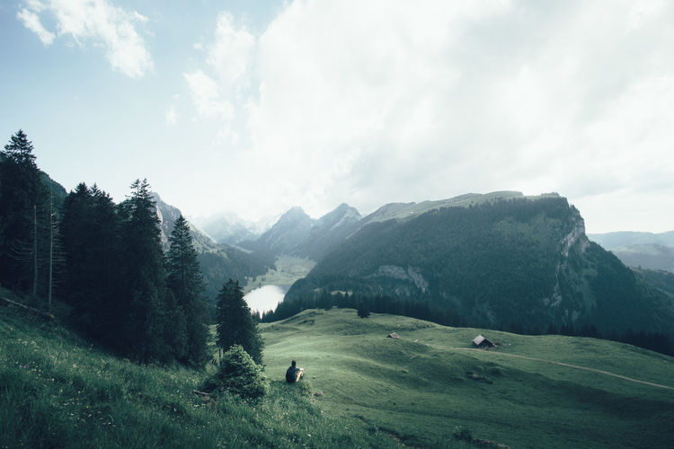 Man sitting on grassy hill against alps