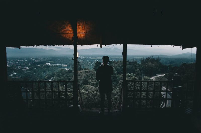 Rear view of silhouette man standing by railing on mountain