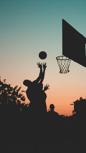 SILHOUETTE PEOPLE PLAYING BASKETBALL AGAINST CLEAR SKY DURING SUNSET