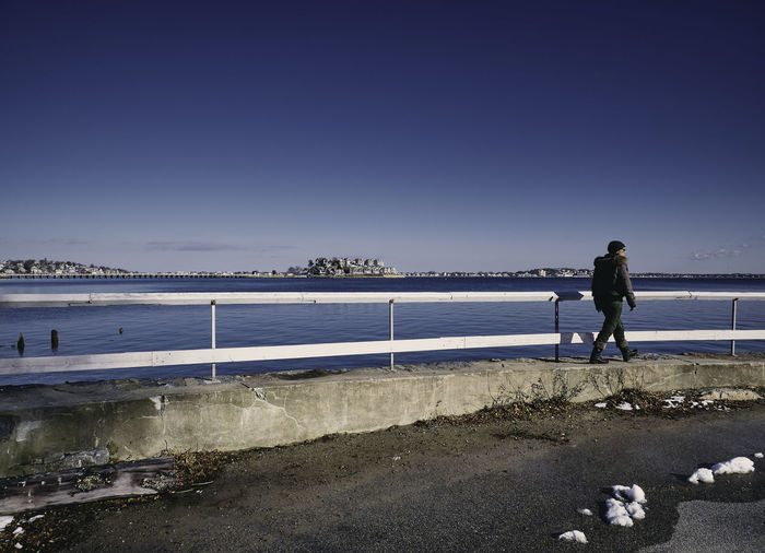 Man walking by sea in city against sky