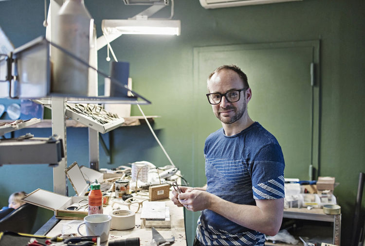 Portrait of confident male owner standing at eyeglasses workshop