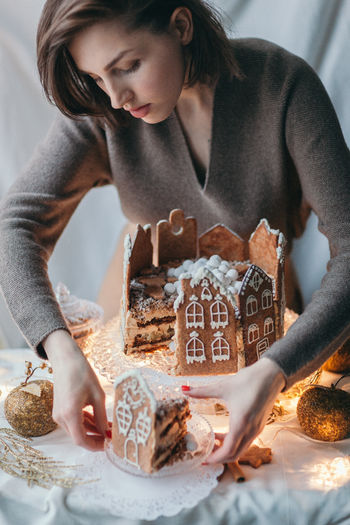 Beautiful young woman arranging gingerbread house on table