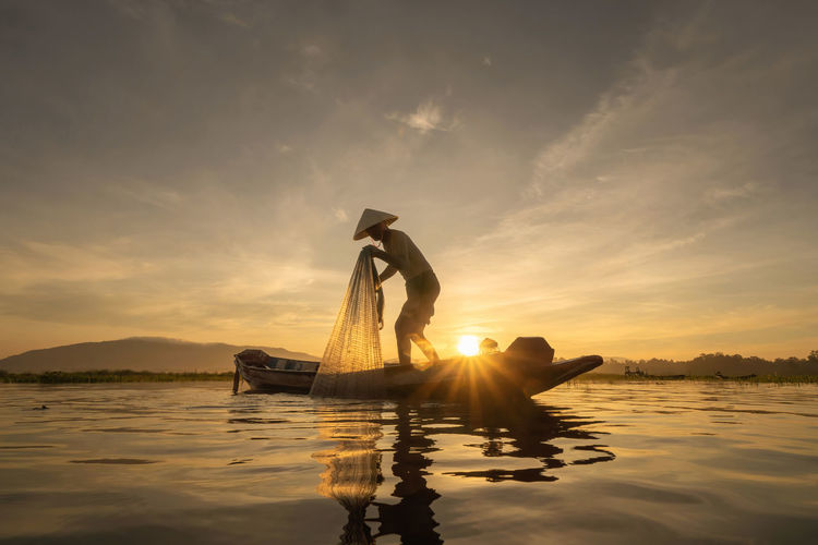 People in lake against sky during sunset