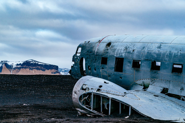Abandoned military airplane at beach against cloudy sky during winter