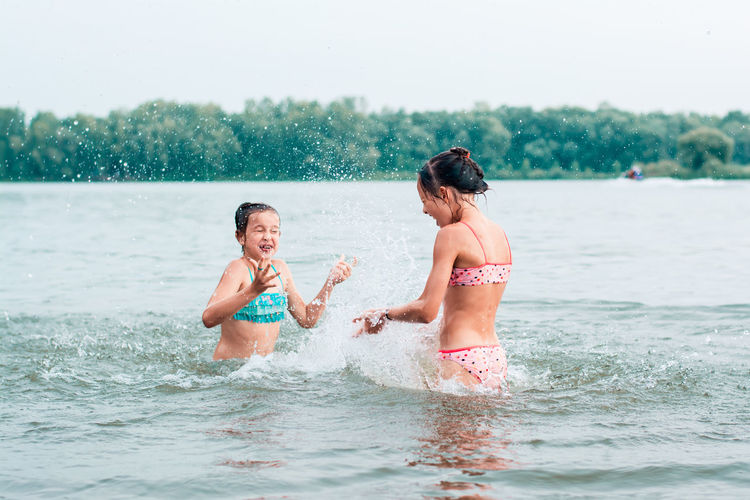 Two teenage girls are splashing each other in the river. local tourism. summer vacation