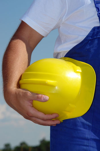 Midsection of man holding hardhat while standing against sky