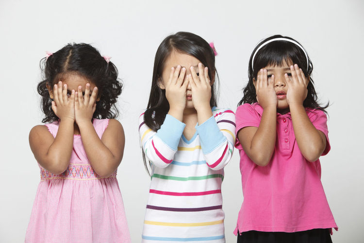 Portrait of girls covering eyes while standing against white background
