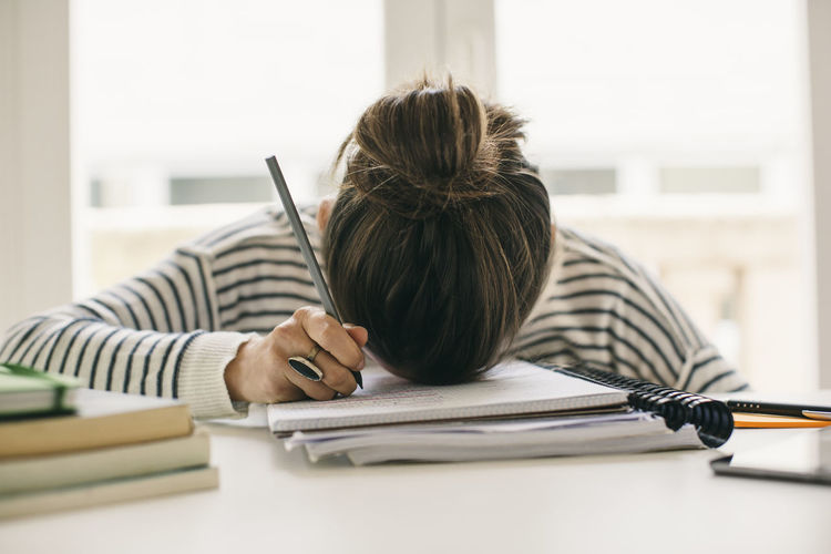 Woman writing on notepad resting her head on table