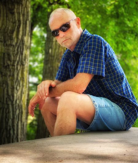 Man wearing sunglasses sitting on plant against trees