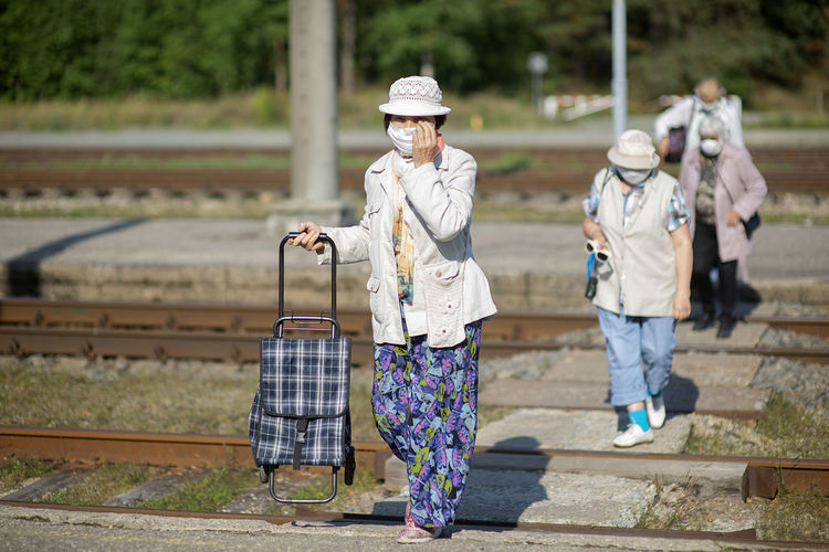 A group of senior travelers with masks on their faces cross the railway tracks