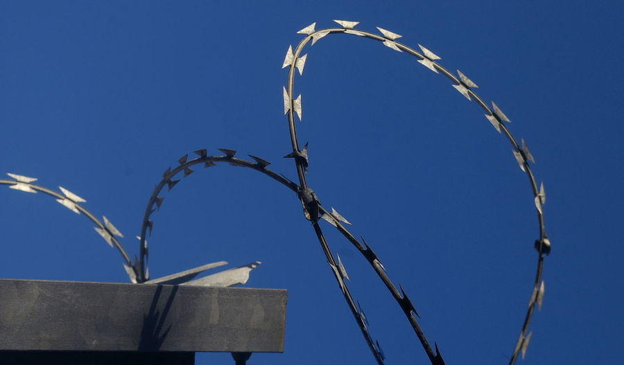Low angle view of razor wires against clear blue sky